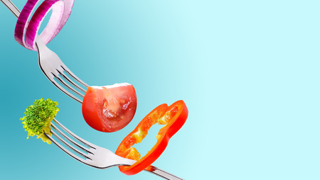 Concept diet and healthy eating background. Fresh broccoli, slices of red pepper, broccoli and tomato on a forks.の写真素材