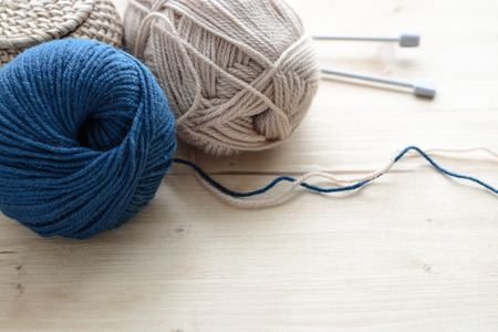 Blue ang beige knitting yarn clews with needles on wooden table