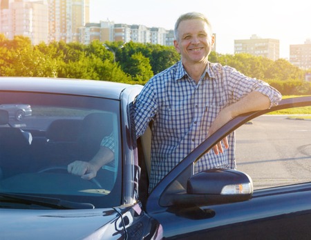 Smiling man standing and leaning on the car doorの写真素材