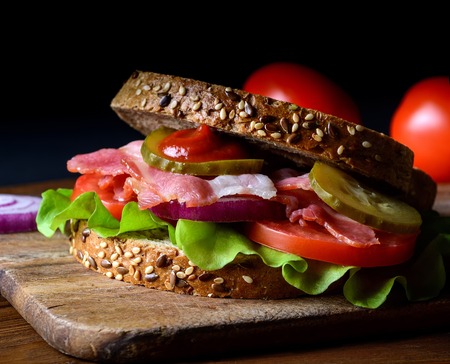 Sandwich freshly prepared with bacon, tomato, cucumber, onion on whole grain wheat toastの写真素材