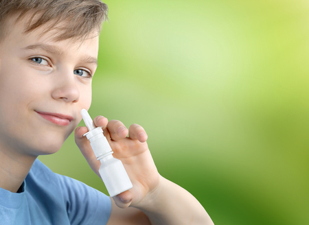 A boy of twelve years old sprays nasal spray on a green blurred background.の写真素材