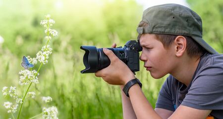 Boy holding digital camera and shooting butterfly on the wild flowerの写真素材
