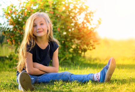 Smiling little blond girl with long hair sitting on the grassの写真素材