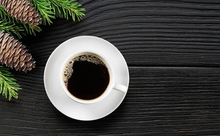 White Coffee cup and christmas tree branch with cones on black wooden background