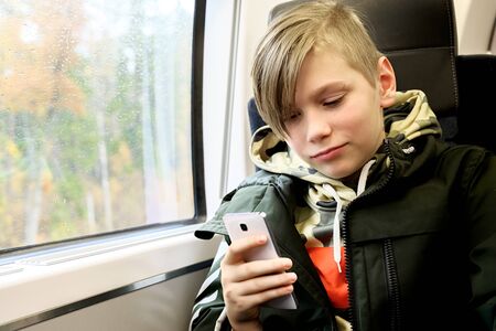 Teenage boy using his smartphone sitting near the window in train.