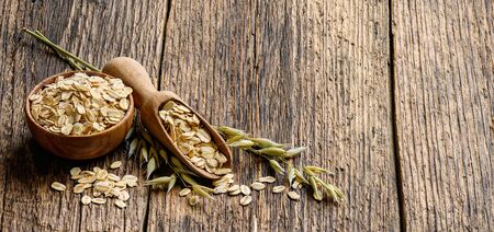 Oat flakes in the bowl with Wooden scoop and oat plant on old wooden table.
