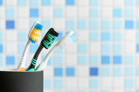 Toothbrushes close-up in a black glass in the blue bathroom background.
