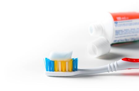 Toothbrush with white toothpaste and tube of toothpaste over white background. Close-up.