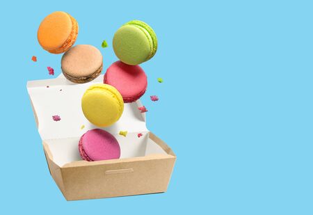 Colorful macaroons falling in paper box over blue background. Copy space.の写真素材