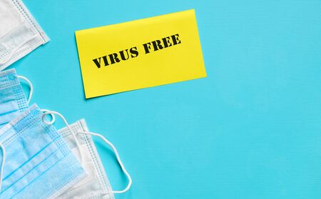 Medical breathing masks for protection against coronavirus VIRUS FREE lettering on yellow paper on blue table background. Top view. Copy spaceの写真素材