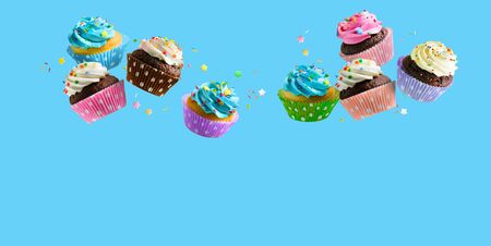 Cupcakes with pink white and blue cream and colorful sprinkles flying over blue background. Copy spaceの写真素材