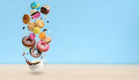 Donuts, cupcakes, cookies, macaroons and coffee cup flying over blue background. . Sweetshop and coffeeshop concept background. Copy space.の写真素材