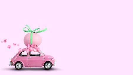 Pink toy car carrying an easter egg on the roof on a pink background.の写真素材