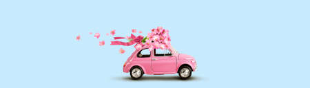 Pink car with bouquet of flowers with ribbon and bow on blue background. Copy space.の写真素材
