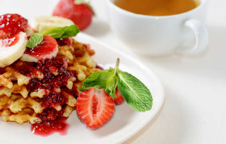 Waffles dessert with strawberries bananas and mint. Cup of tee for healthy breakfastの写真素材