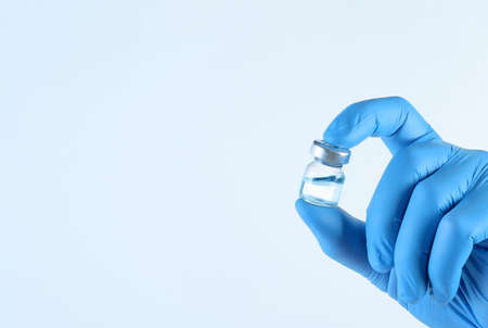 A vial of vaccine for injection in the doctors hand on a light blue backgroundの写真素材