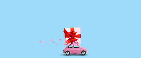Pink car with gift box on a roof with flowers on a blue background.