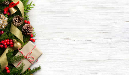 Christmas border composition made of fir branches, cones and gift box on white wooden backgroundの写真素材