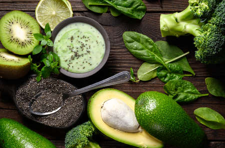 Green smoothie with Healthy ingredients: avocado, spinach, kiwi, chia seeds on wooden table.