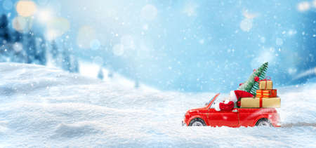Santa Claus in Red car delivering christmas tree and gifts at snowy background. Christmas cardの写真素材