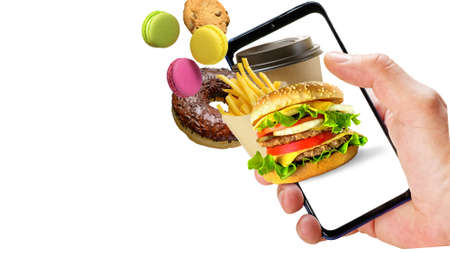 Hand holding phone with hamburger french fries coffee cup donuts flying out of the screen isolated...