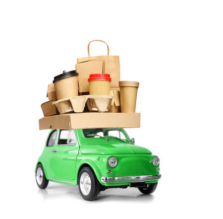 Retro green toy car delivering fast food order - various take-out food containers, pizza box, coffee cups in holder and paper bag isolated on whiteの写真素材
