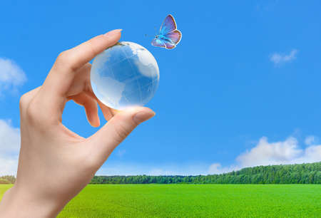Glass globe of the planet Earth in human hand and flying butterflyの写真素材