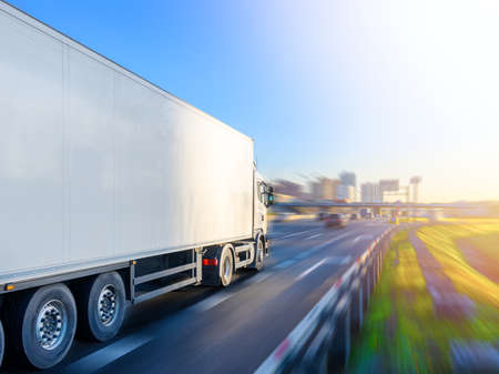 A big truck with a white trailer driving towards a city