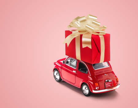Red toy car with gift box on a roof on pink background. Copy space.の写真素材