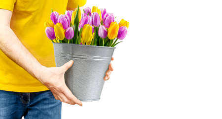 Courier delivers flowers and holds a bucket of tulips in his hands on whiteの写真素材