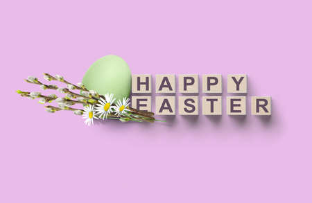 HAPPY EASTER on wooden cubes concept background with egg, willow and daisies