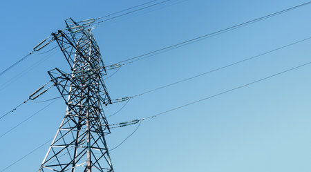 Steel power pylon construction with high voltage cables against blue sky.