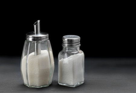 Sugar dispenser and and glass Salt shaker on slate black stone backgroundの写真素材