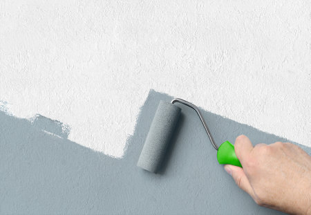Man applying grey paint with roller brush on white wall, copy spaceの写真素材