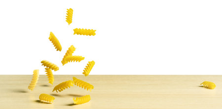 Raw Pasta fusilli falling on a wooden table on whiteの写真素材