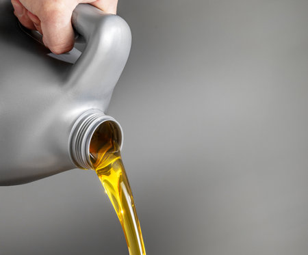 Carefully Pouring Engine Oil from a Gray Plastic bottle for Automotive Maintenance and Serviceの写真素材