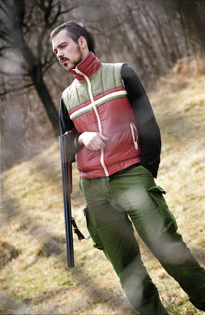 A hunter stands leisurely, his rifle hanging from his arm as he looks in the distance.