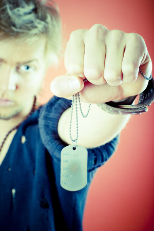 A victorious tough guy stares at the identification tags in his clenched fist belonging to someone else. Color digitally processed.の写真素材