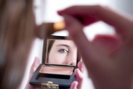 Mid adult woman applying make-up in the mirror; eye reflectionの写真素材