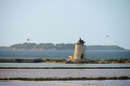 Traditional salt manufacturing windmill with kite surfer in the background, Saline di Trapani, Sicily, Italyの写真素材