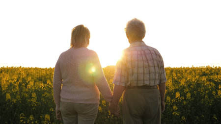 Elderly Couple Holding Hands Standing In A Blooming Field At Sunsetの写真素材