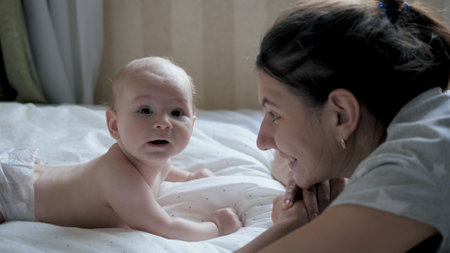 Caucasian Mom Talks To Her Funny Newborn Baby Lying On The Bedの写真素材