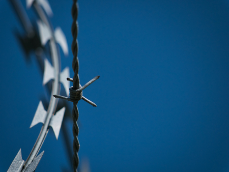 A pointy barbed wire and a sharp blade wire with blue sky as backgroundの写真素材