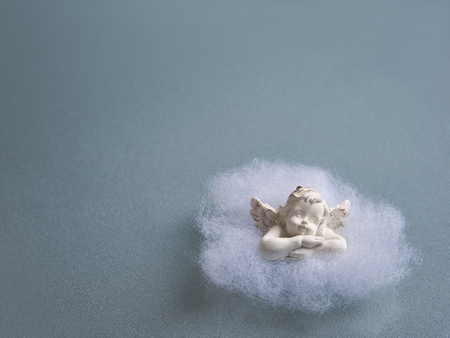 A little angel in cotton wool on a blue-grey glass plate made of frosted glassの写真素材