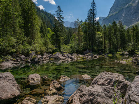 Boulders in crystal clear lake in alps surrounded by forest