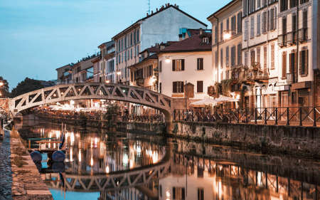 Bridge Pont de fer across water of Naviglio Grande grand canal waterway, embankment, promenade and colourful building at sunsetのeditorial素材