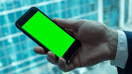 Businessman is holding black smartphone with green screen near the window in officeの写真素材