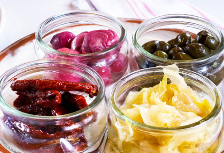 Variety of pickled vegetables in glass jars on a white background