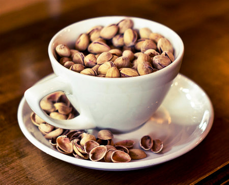 Pistachios in a white cup on a wooden table.の写真素材