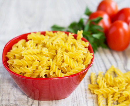 Raw fusilli pasta in a red bowl on a wooden tableの写真素材